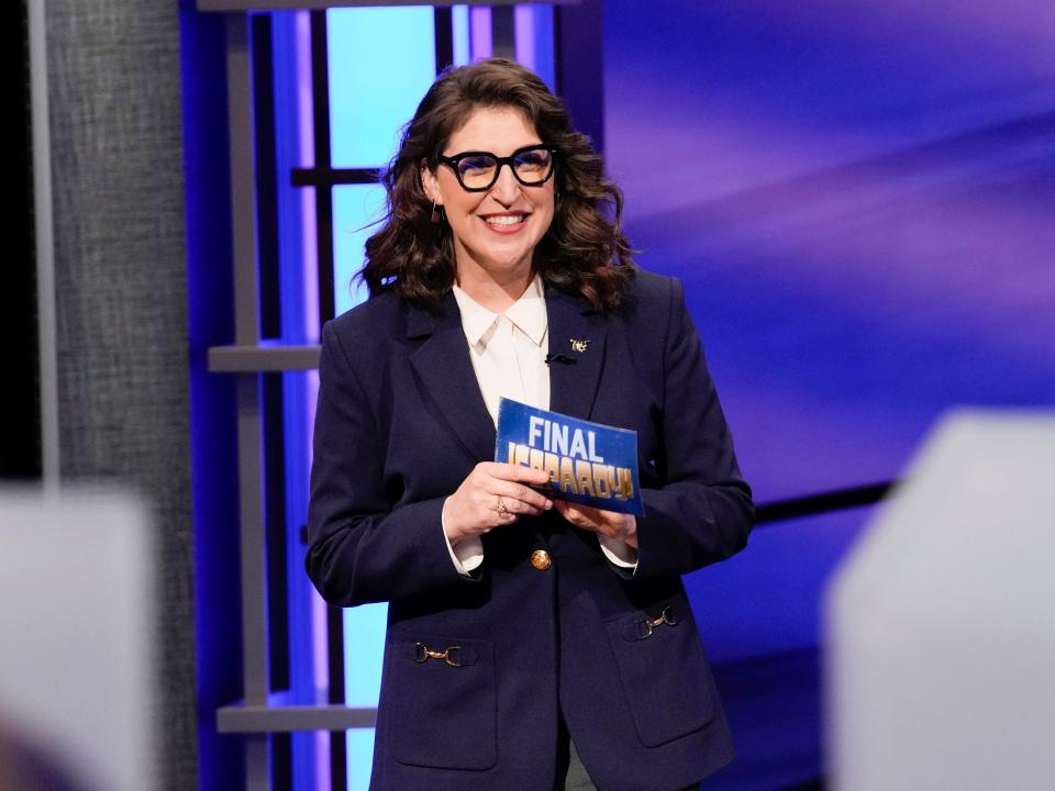 Mayim Bialik, wearing a purple blazer, hosts the "Jeopardy!" National College Championship