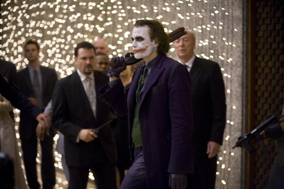 The Dark Knight - 

Medium shot of Heath Ledger as Joker at party holding gun with crowd in background including Michael Caine as Alfred.