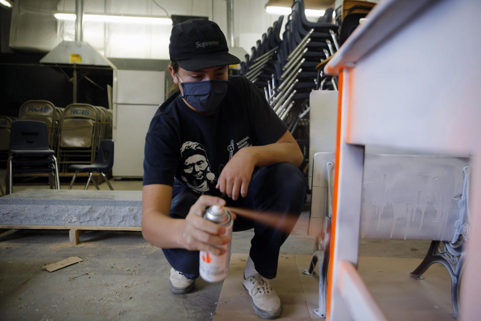 Caden Pourier, a freshman at Red Cloud Indian School, spray-paints a desk orange to bring awareness to the abuse and cultural loss experienced by Indigenous students forced to attend residential schools from the late 19th to the mid-20th centuries, on Sept. 29, 2021, in Pine Ridge, S.D. The 133-year-old school, formerly known as Holy Rosary Mission, has begun what it calls a Truth and Healing process to confront past abuses and create ways for community members to heal from their trauma. (AP Photo/Emily Leshner)