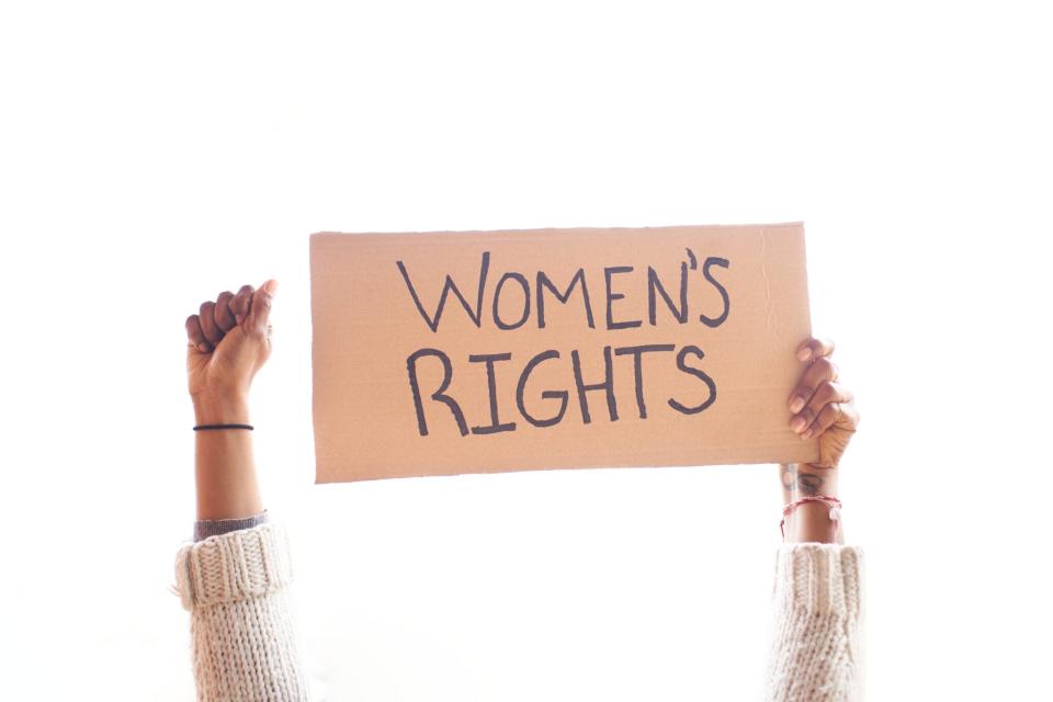 Isolated banner holded by a black woman, and her fist up in a white background, and written: Women's rights.