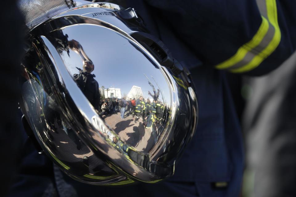 Firefighters as reflected on a firefighter helmet during a protest outside parliament amid a contract dispute with the cash-strapped government, in Athens on Thursday, Feb. 16, 2017. The government says it is lacking the funds needed to offer thousands of firefighters long-term contracts. Greece is under pressure to make deeper spending cuts as it struggles to reach agreement with bailout lenders on the terms of future loan payouts. (AP Photo/Thanassis Stavrakis)