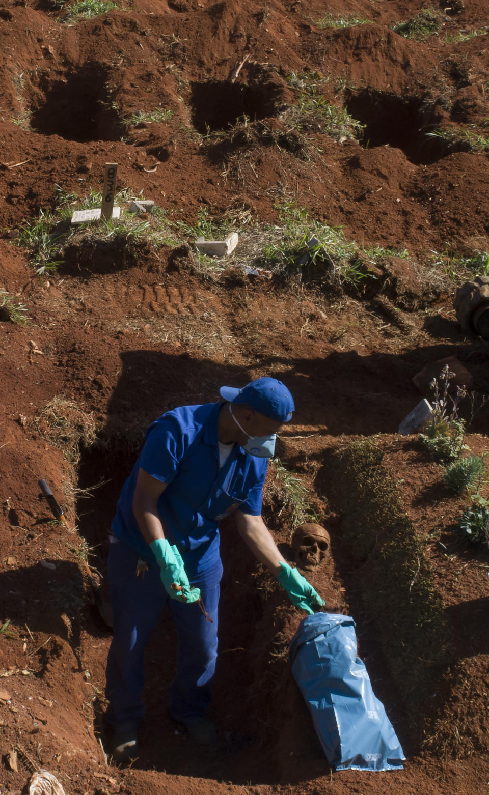 Un trabajador exhuma el cuerpo de una persona enterrada hace tres años en el cementerio de Vila Formosa, que no cobra a las familias por las tumbas, en Sao Paulo, Brasil, el 12 de junio de 2020. Los cuerpos sepultados hace al menos tres años, se exhuman y almacenan en bolsas de plástico para dejar sitio a más féretros, una necesidad más acuciante en la pandemia del coronavirus. (AP Foto/Andre Penner)