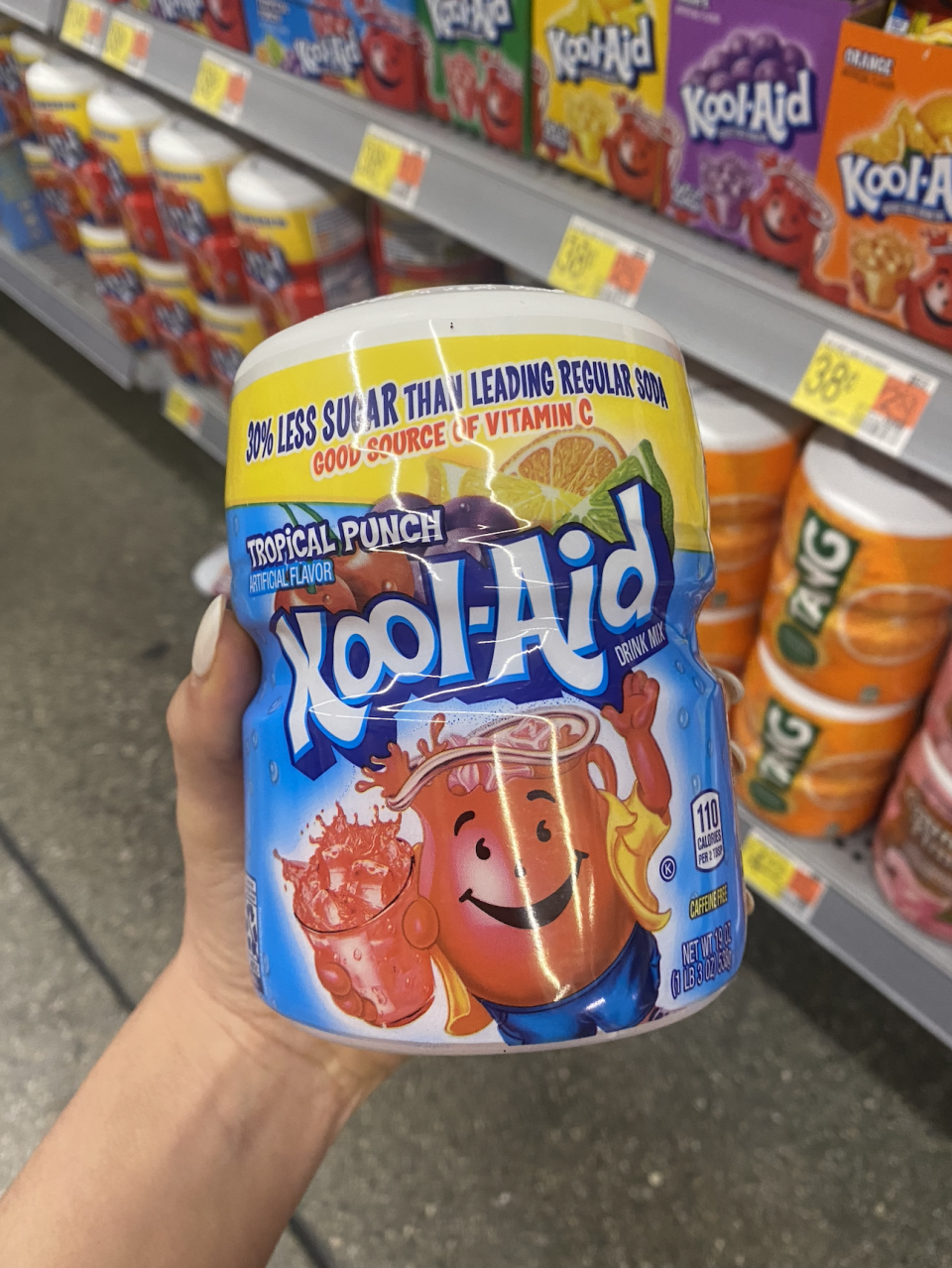 Hand holding a container of Tropical Punch Kool-Aid. Container states 