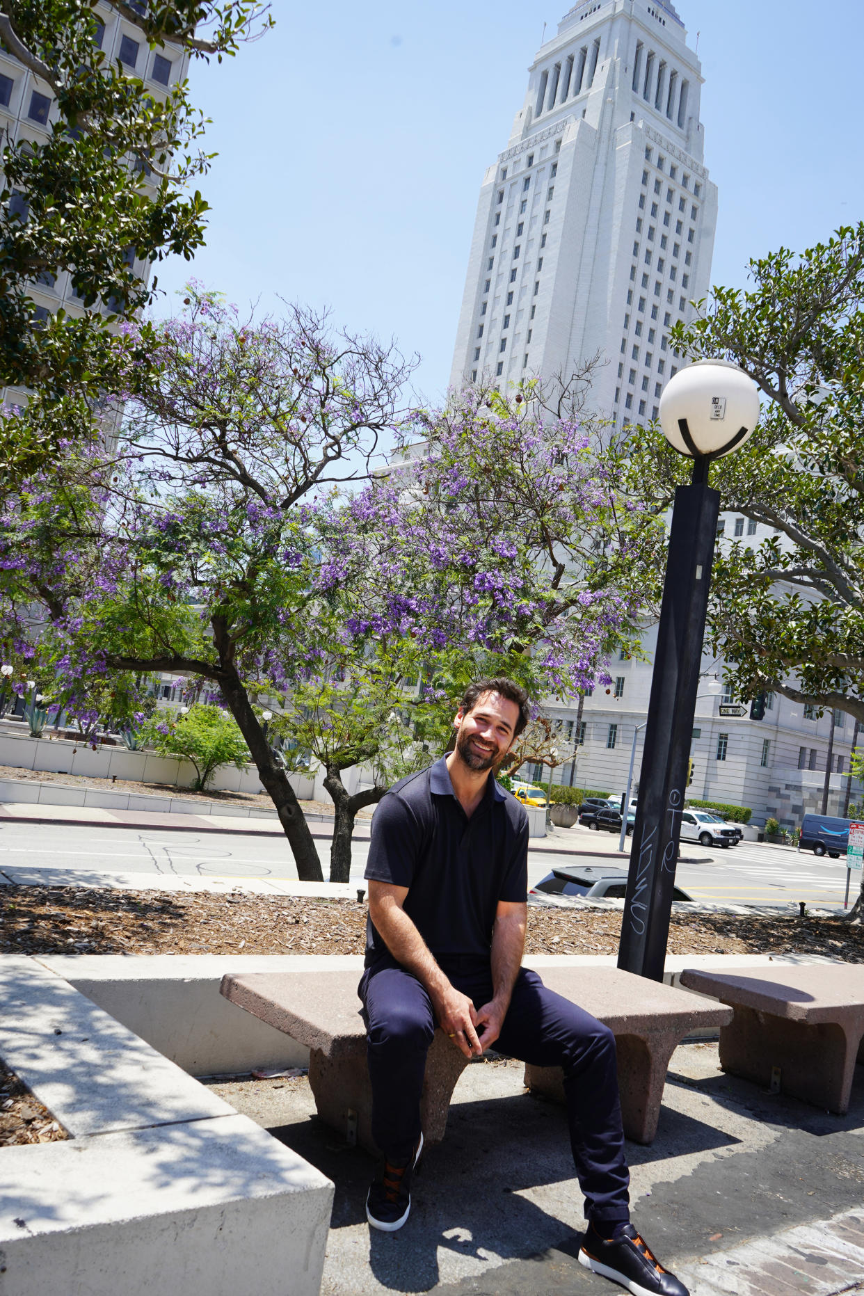 Manuel Garcia-Rulfo sits on a bench in Downtown Los Angeles in front of a flowering purple tree and white art deco building (Samantha Kubota / TODAY)