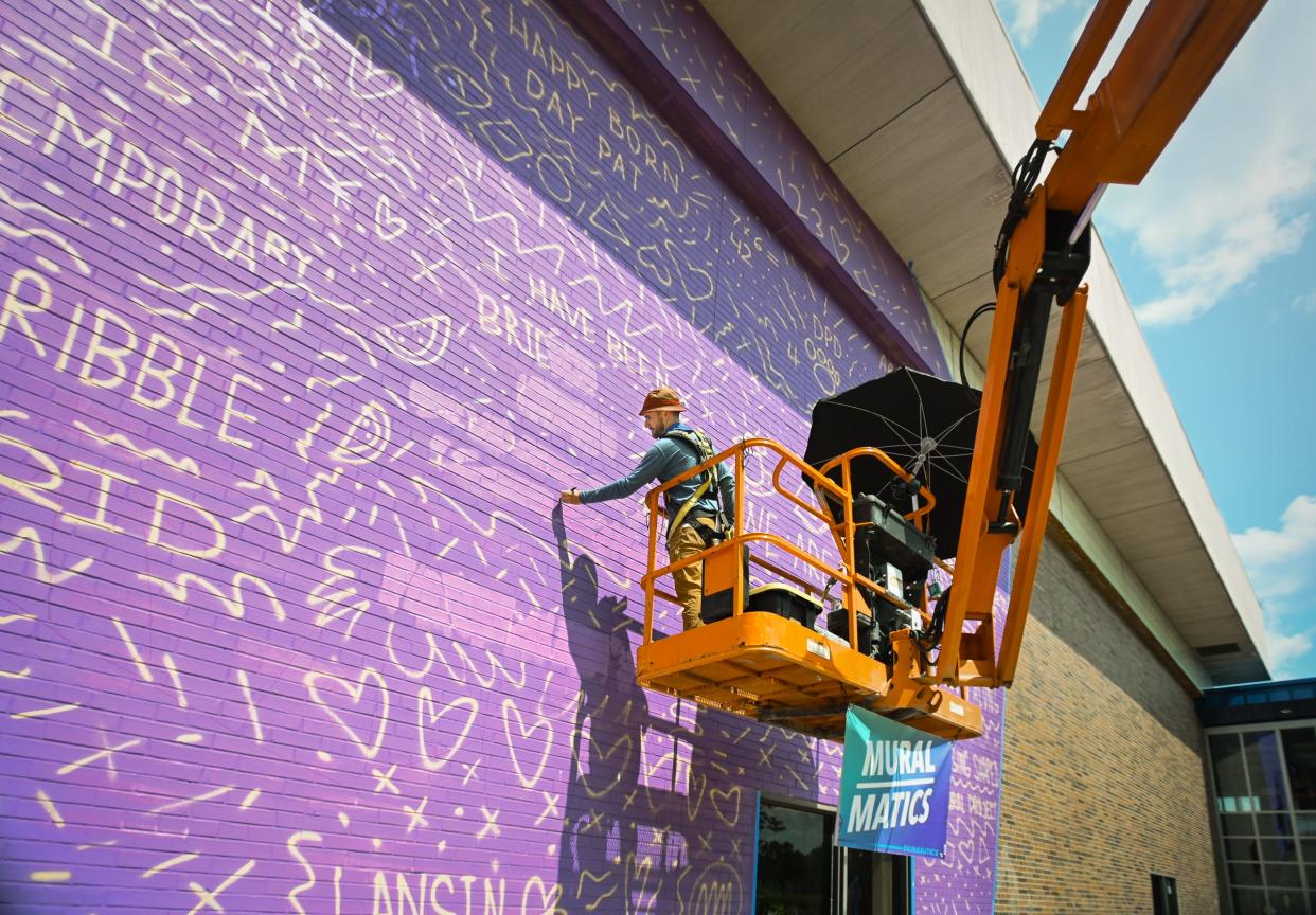 Artist Dustin Hunt of Muralmatics demonstrates one of the steps in his mural-making process, Wednesday, Aug. 14, 2024, at the Alfreda Schmidt Community Center, formerly Harry Hill High School on Lansing's southside. Hunt's three-part project titled "Lansing Shaped" will depict three generations of a Lansing family - children, parents, and grandparents, at three different schools.