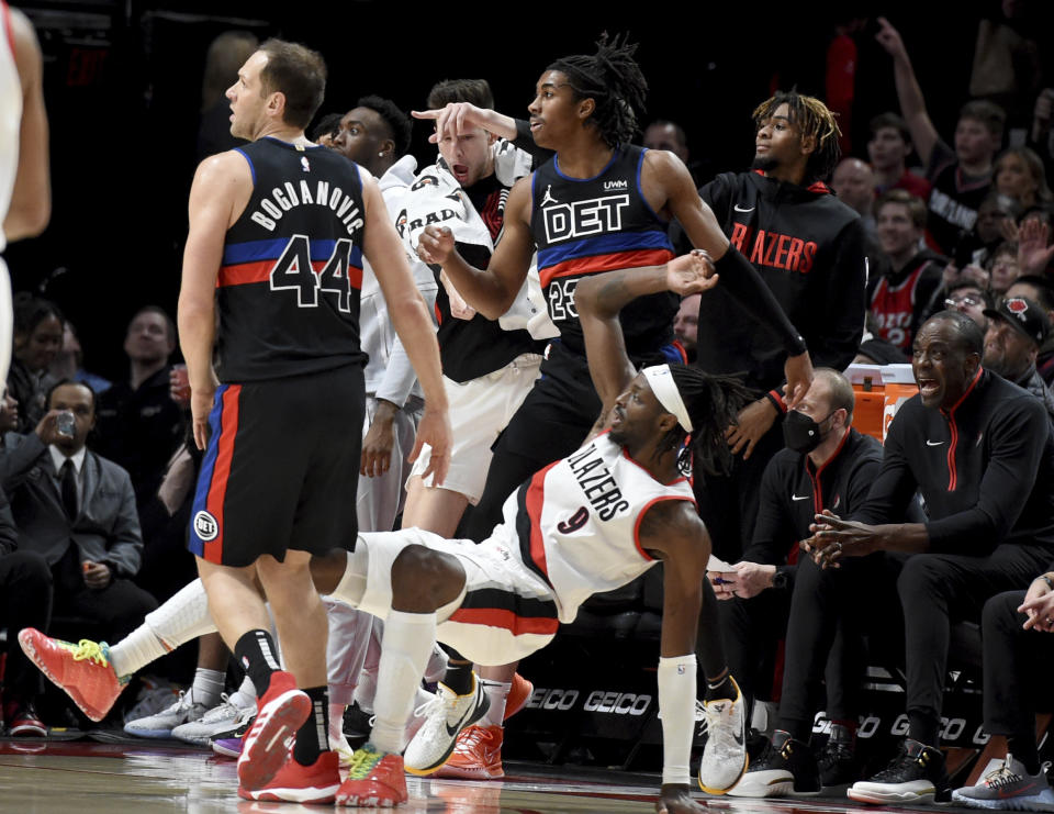 Portland Trail Blazers forward Jerami Grant, bottom, watches as he hits a shot while falling down in front of the Blazers bench, as Detroit Pistons forward Bojan Bogdanovic, left, and guard Jaden Ivey, top, look on during the second half of an NBA basketball game in Portland, Ore., Monday, Jan. 2, 2023. (AP Photo/Steve Dykes)