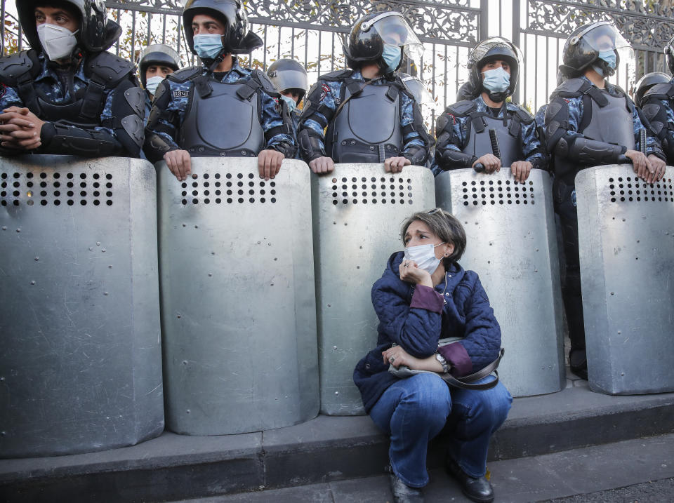 A woman sits as police guard during a protest against an agreement to halt fighting over the Nagorno-Karabakh region, in Yerevan, Armenia, Wednesday, Nov. 11, 2020. Thousands of people flooded the streets of Yerevan once again on Wednesday, protesting an agreement between Armenia and Azerbaijan to halt the fighting over Nagorno-Karabakh, which calls for deployment of nearly 2,000 Russian peacekeepers and territorial concessions. Protesters clashed with police, and scores have been detained. (AP Photo/Dmitri Lovetsky)