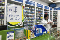 FILE - In this Tuesday, Jan. 21, 2020, file photo, pharmacist Liu Zhuzhen stands near a sign reading "face masks are sold out" at her pharmacy in Shanghai, China. Panic and pollution drive the market for protective face masks, so business is booming in Asia, where fear of the virus from China is straining supplies and helping make mask-wearing the new normal. (AP Photo/Fu Ting, File)