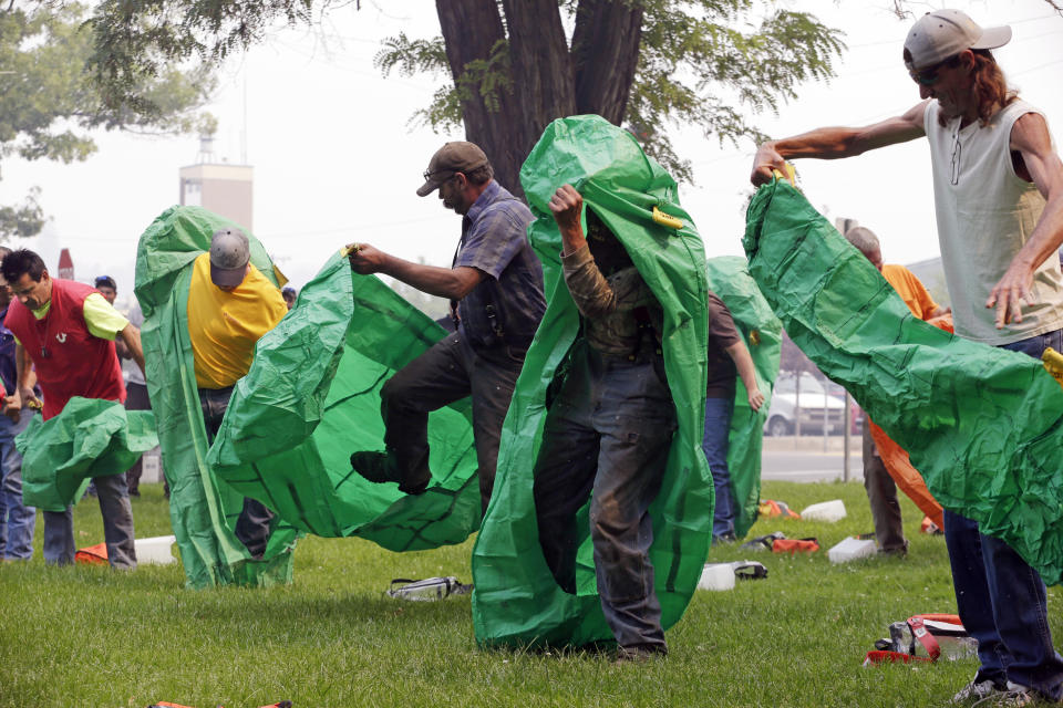 FILE - In this Aug. 22, 2015 file photo, volunteers learn to deploy fire shelters with practice equipment after a callout by fire officials seeking to supplement their usual resources in Omak, Wash. After flames trapped 14 firefighters in California and they had to use last-resort fire shelters to survive, questions are emerging about how well the emergency devices work and how often they are used while crews fight wildfires. (AP Photo/Elaine Thompson, File)