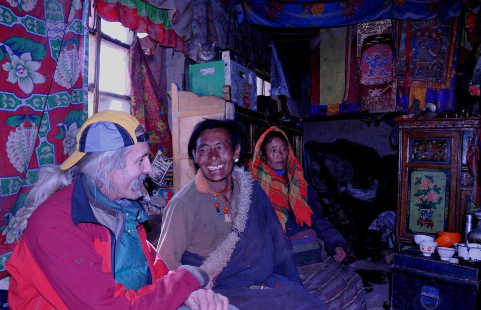 A man in a baseball cap sits with two Tibetans inside their home