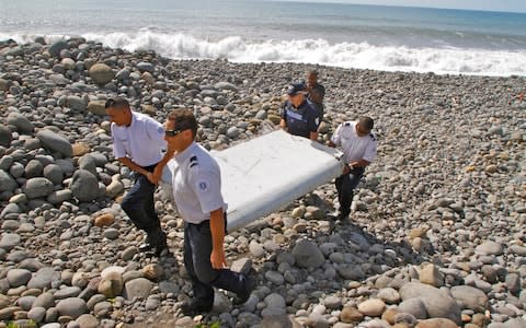 French police officers carry a piece of debris from MH370 in Saint-Andre, Reunion Island - Credit: AP