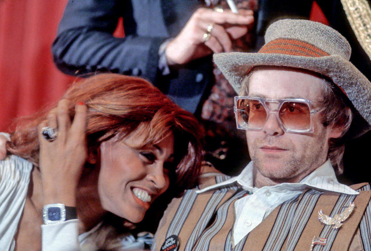 MARCH 18: Rock and roll singer Tina Turner snuggles up to fellow performer Elton John during a press conference  for the release of the rock group "The Who's" rock opera film "Tommy" in which they appear on March 18, 1975. (Photo by Michael Ochs Archives/Getty Images)  