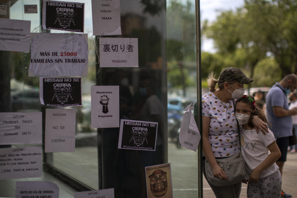 A woman and her daughter stand next to the window of a a car dealerships covered by leaflets during a protest in Barcelona, Spain, Friday, May 29, 2020. Employees in Spain of Japanese giant Nissan took to the streets for the second day in a row to protest the closure of three Barcelona plants as the carmaker scales down its global production. Hundreds of workers have surrounded at least four of Nissan's car dealerships on Friday in or around the northeastern city, covering their windows with leaflets reading "Nissan betrays 25,000 families" and "We will keep fighting" among others. (AP Photo/Emilio Morenatti)