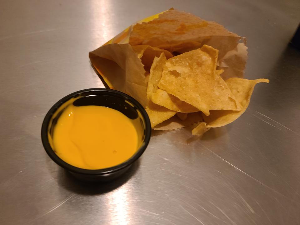 small container of nacho cheese sauce next to a paper bag of tortilla chips from taco bell