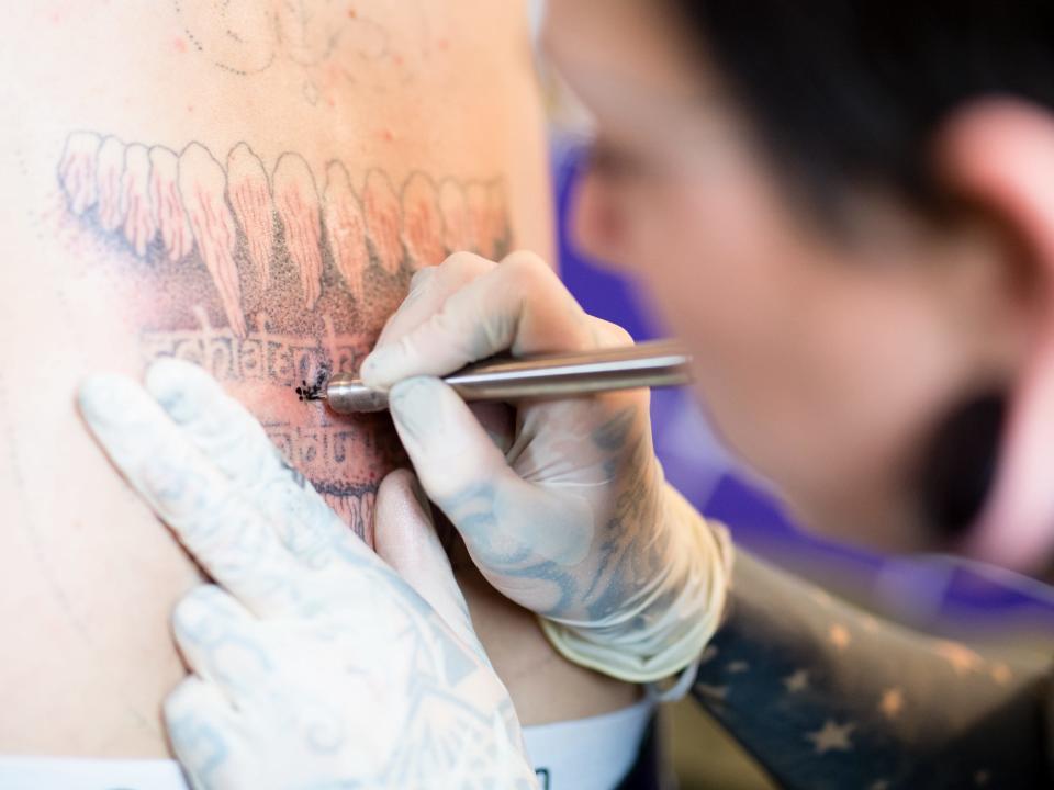 A tattoo artist works on a man’s back with the stick-and-poke method