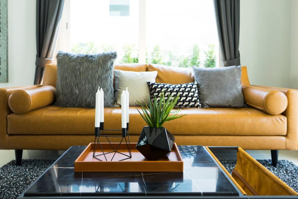 Brown leather sofa near a coffee table with black vase and modern candle holder.