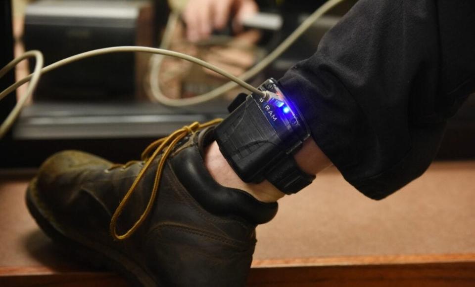 A participant downloads information through an ankle monitor bracelet as part of the 24/7 Sobriety Program.