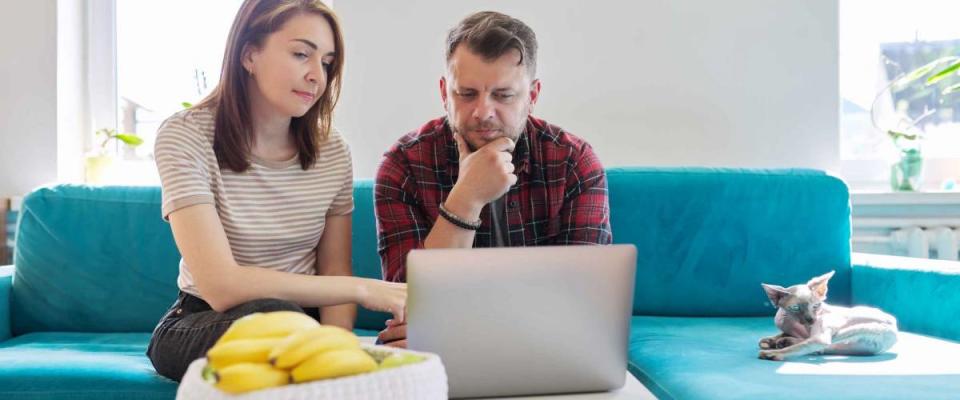 Serious middle-aged couple husband and wife with laptop sitting at home on couch