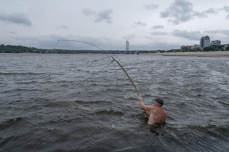 A man fishes on a central beach as water in the Dnipro river dropped more than 4 meters after the explosion of the Kakhovka dam in Zaporizhzhia, Ukraine, Sunday, July 9, 2023. (AP Photo/Evgeniy Maloletka)