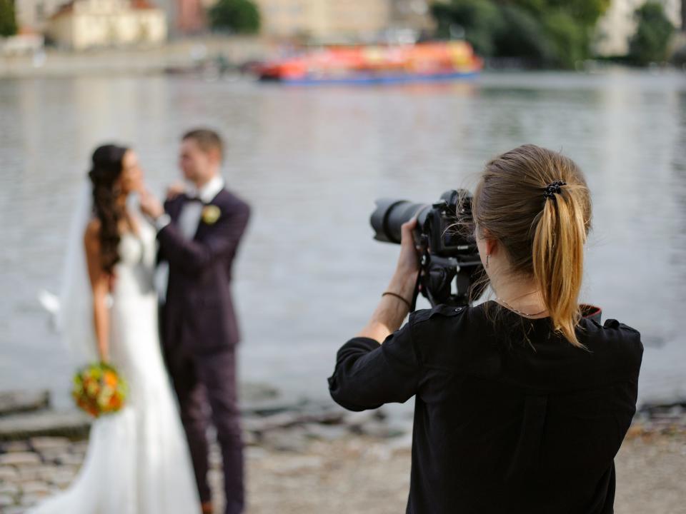 photographer taking pictures of bride and groom by water