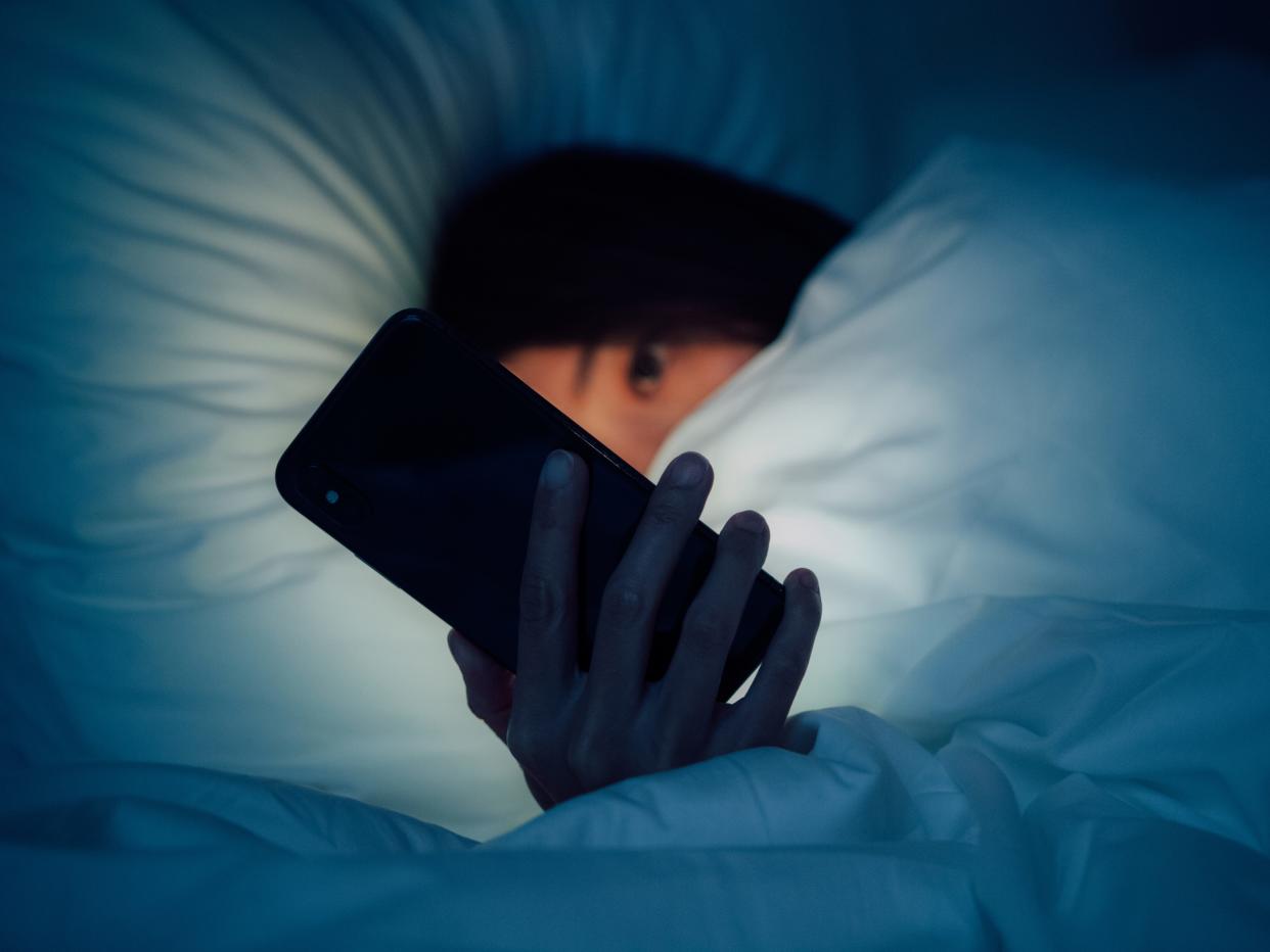 Woman hiding under the blanketed and using smart phone at late night on bed