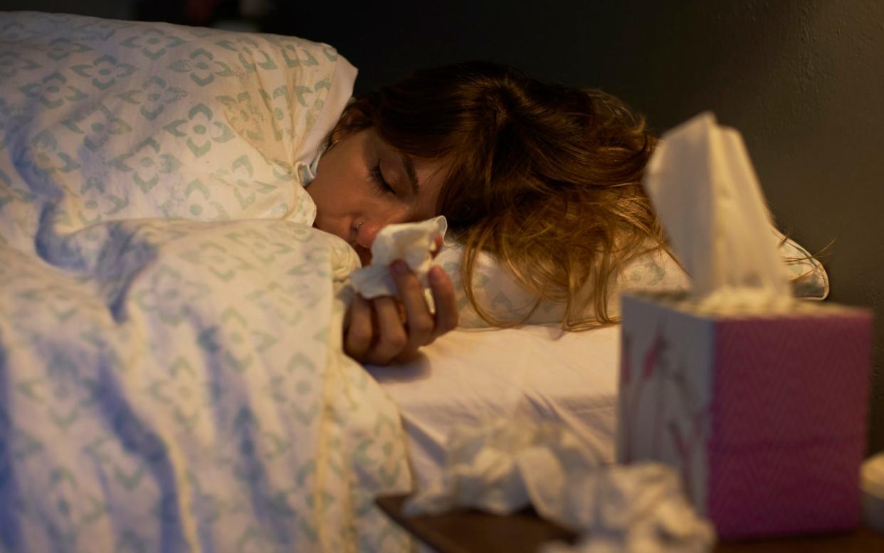 Woman with cold lying down in bed holding tissues