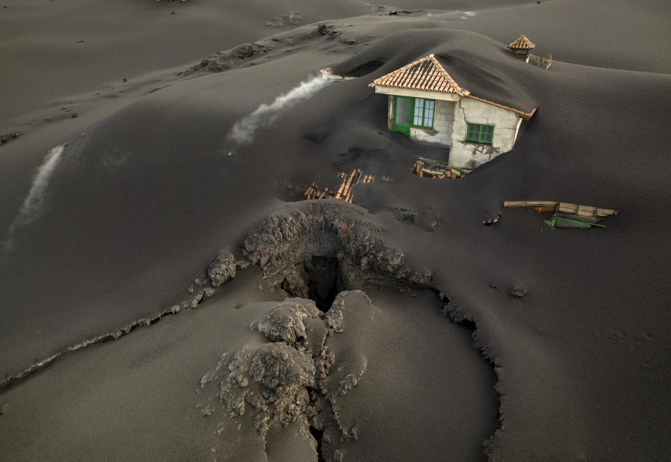 FILE - A fissure is seen next to a house covered with ash on the Canary island of La Palma, Spain, Dec. 1 2021. Authorities on a Spanish island are declaring a volcanic eruption that has caused widespread damage but no casualties officially finished, following ten days of no significant sulfur dioxide emissions, lava flows or seismic activity. But the emergency in La Palma, the northwesternmost of the Atlantic Ocean's Canary Islands, is not over yet, said the director of the archipelago’s volcanic emergency committee, or Pevolca, Julio Pérez. (AP Photo/Emilio Morenatti, File)