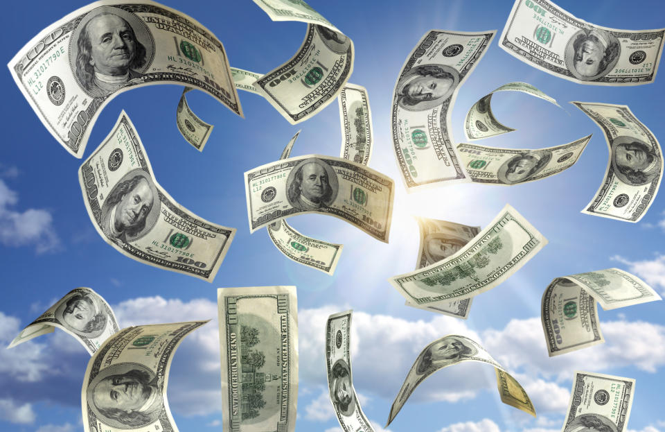 Hundred-dollar bills fly around against a blue sky.