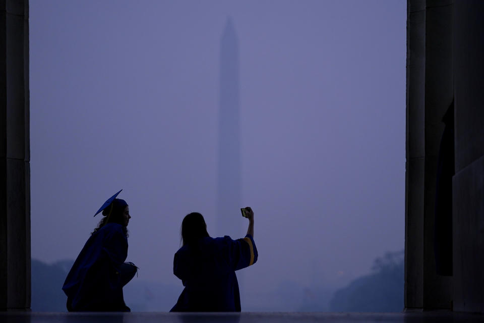 Catalina Kramlich Roldan, left, and Grace Enders, wearing their cap and gown to celebrate their graduation from Robinson Secondary School in Fairfax, Va., pose for a selfie at the steps of the Lincoln Memorial as a thick layer of smoke and the Washington Memorial give backdrop to them, Thursday, June 8, 2023, in Washington. Intense Canadian wildfires are blanketing the northeastern U.S. in a dystopian haze, turning the air acrid, the sky yellowish gray and prompting warnings for vulnerable populations to stay inside. (AP Photo/Julio Cortez)