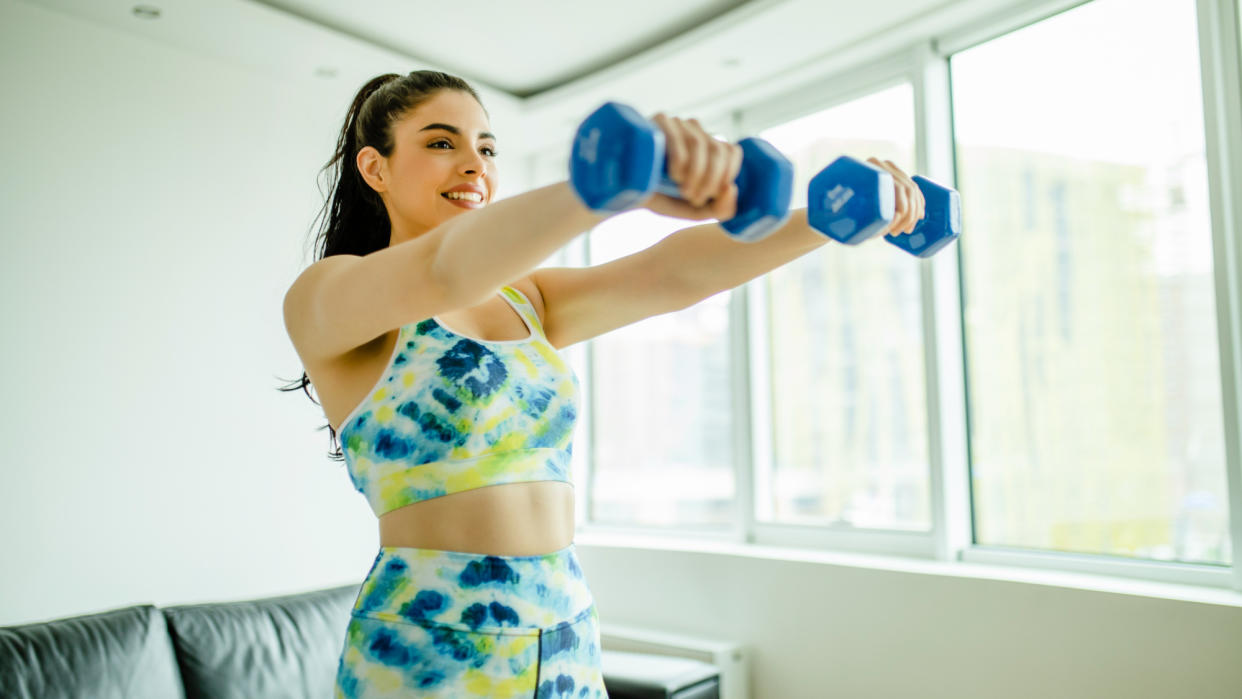  A woman completing an upper-body dumbbell workout at home. 