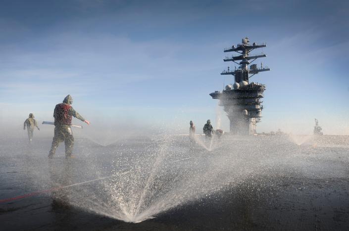 Sailors participate in a countermeasure wash down on the flight deck of the aircraft carrier USS Nimitz