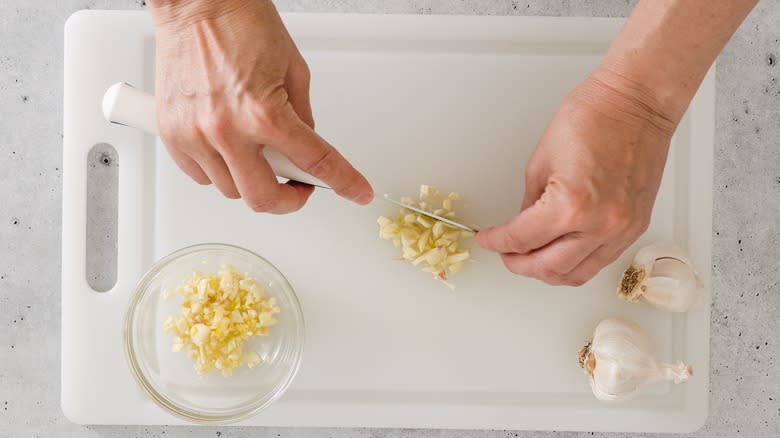 person mincing garlic on board