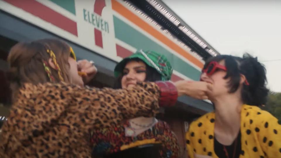 Three girls from the band Froggy eat nachos outside a 7-Eleven