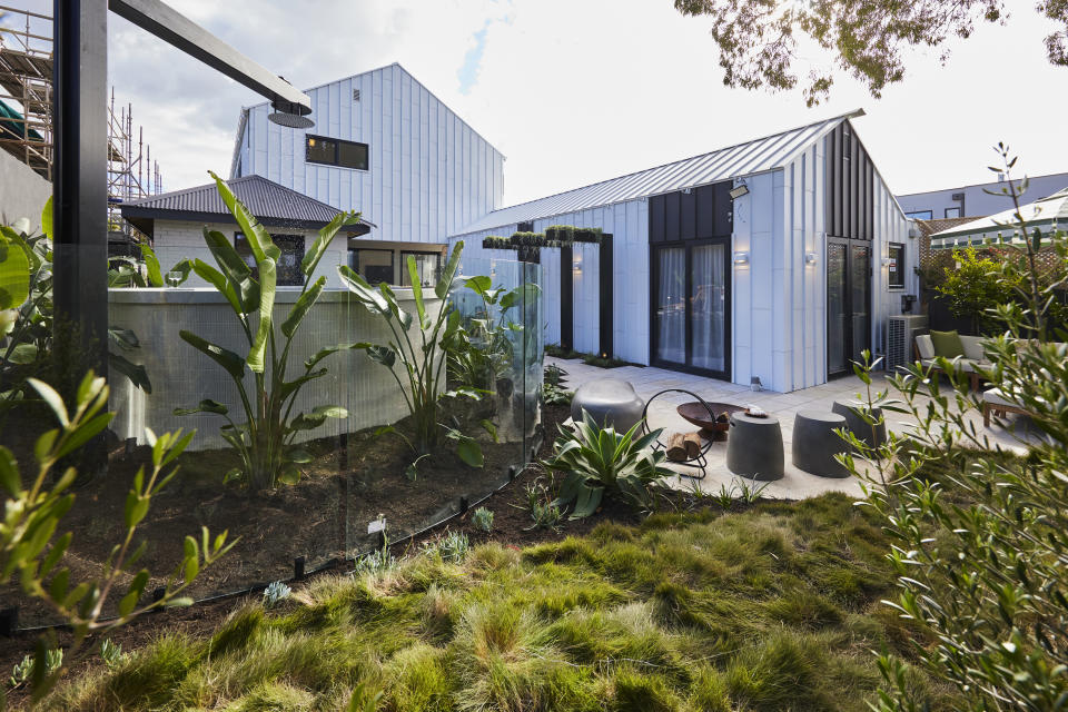 A wide shot of the backyard with the pool on the left, a planted area at the front and the side of the house. 