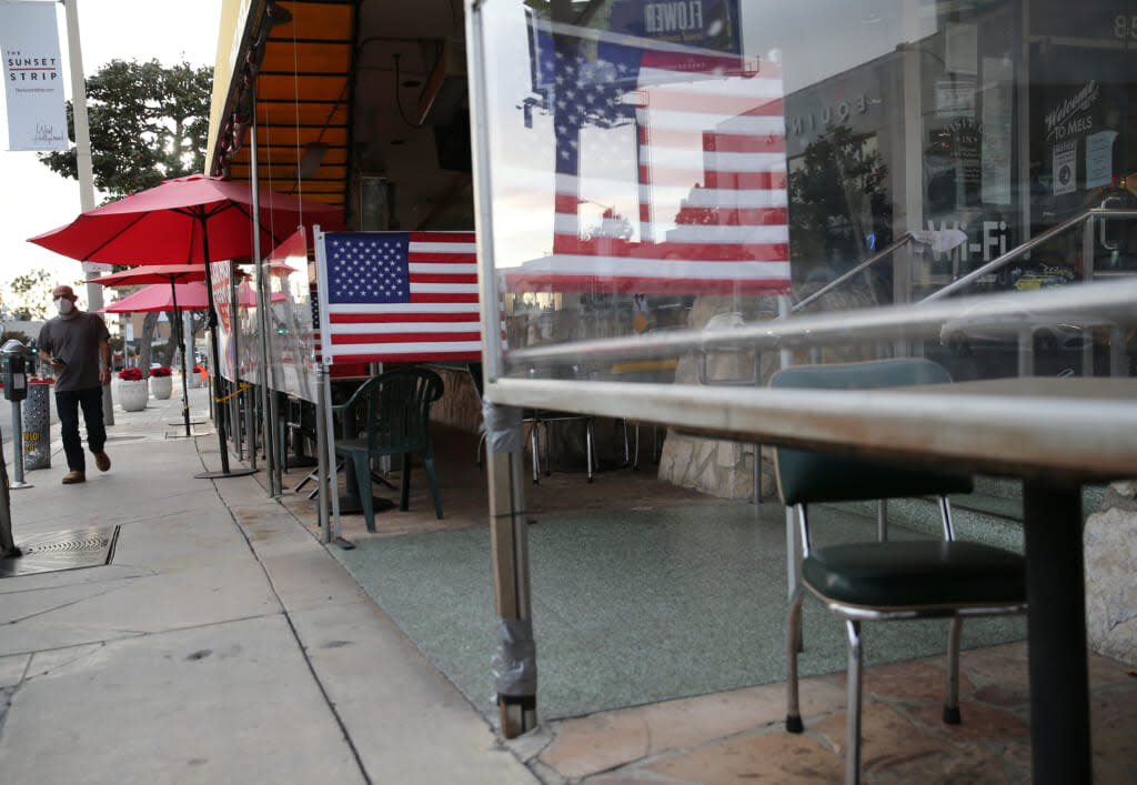 A man walks past shuttered outdoor restaurant seating decorated with American flags on the first day of new stay-at-home orders on December 7, 2020 in West Hollywood, California. (Photo by Mario Tama/Getty Images)