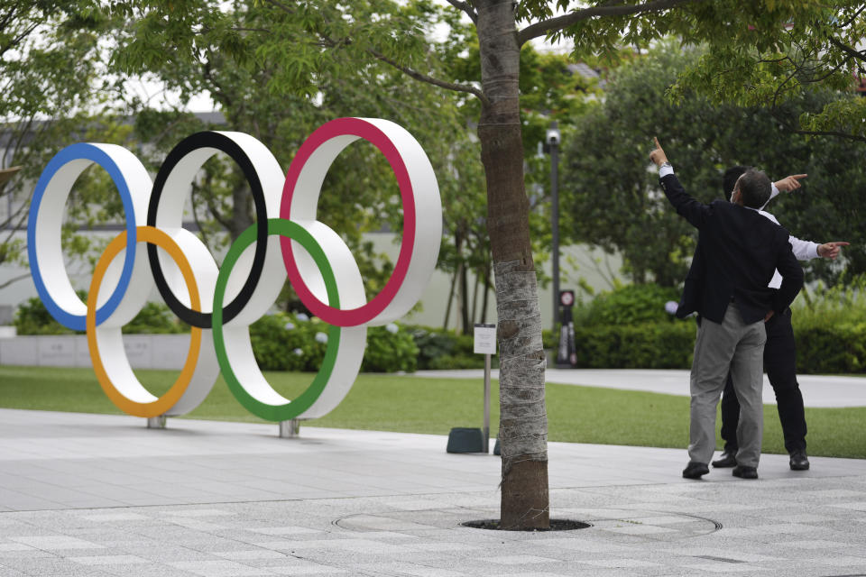 FILE - In this June 2, 2021, file photo, men gesture near the Olympic Rings, in Tokyo. Public sentiment in Japan has been generally opposed to holding the Tokyo Olympics and Paralympics. This is partly based of fears the coronavirus will spike as almost 100,000 people — athletes and others — enter for both events.(AP Photo/Eugene Hoshiko, File)