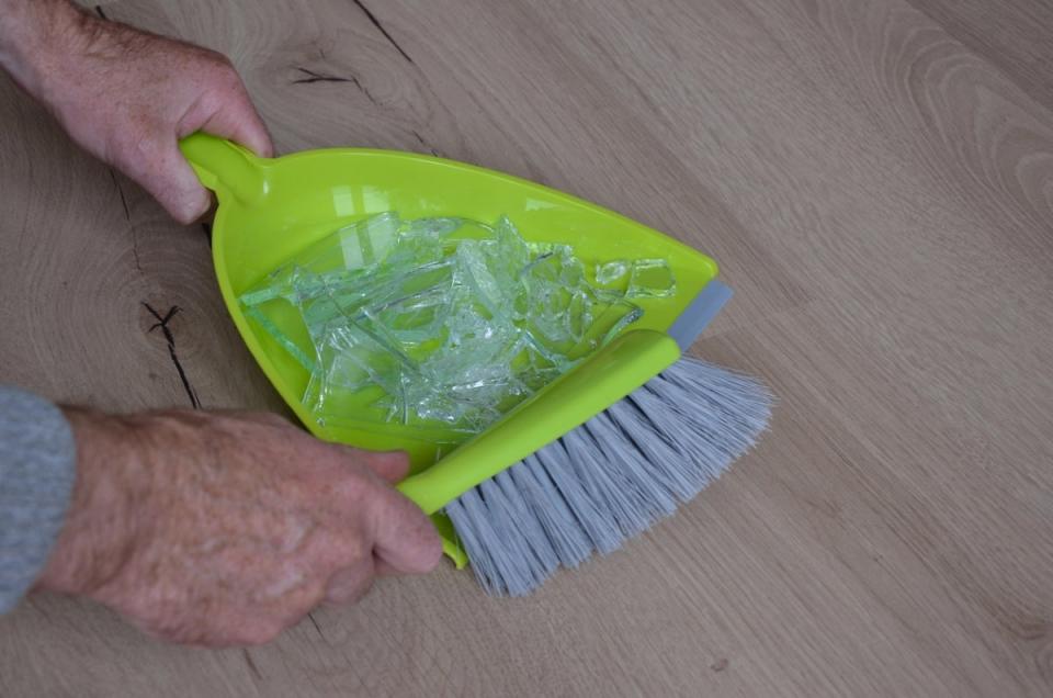 Man sweeping broken glass into a neon green dustpan.