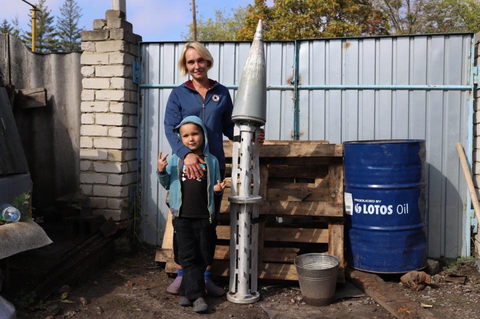 Tatiana and her son, eight, stand next to a rocket fired into their vegetable garden in Kun’je near Kharkiv (Tom Mutch)