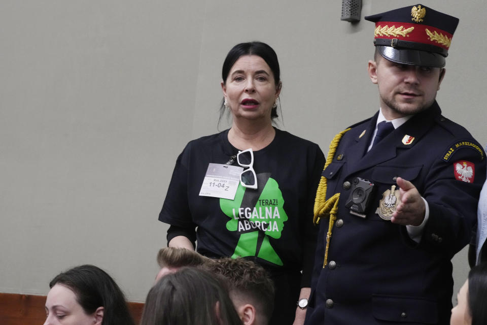 An activist wearing a T-shirt that says "Legal Abortion Now!" is guided to her place by a guard as she attends a debate in parliament on liberalizing the Polish abortion law in Warsaw, Poland, on Thursday April 11, 2024. The traditionally Catholic nation has one of the most restrictive laws in Europe. The reality is that many women terminate pregnancies at home with pills mailed from abroad. (AP Photo/Czarek Sokolowski)