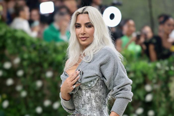 Kim Kardashian poses outdoors in a form-fitting floral-patterned dress with an off-the-shoulder cardigan