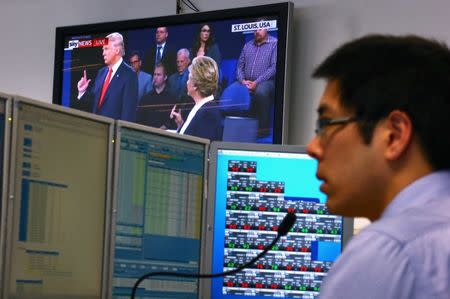 A trader works at his desk as the U.S. presidential town hall debate between Republican U.S. presidential nominee Donald Trump and Democratic nominee Hillary Clinton is shown on television at Citibank's trading floor located in central Sydney, Australia, October 10, 2016. REUTERS/David Gray