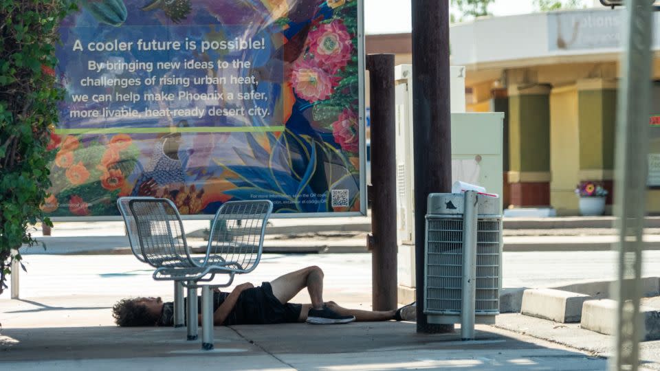 An unhoused man finds little respite from the heat in the shade of a bus stop in Phoenix. - Julian Quinones/CNN