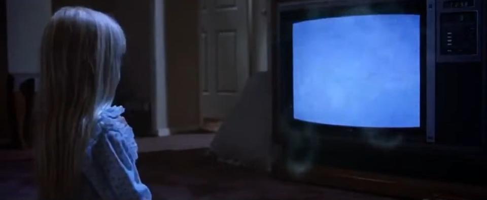 Carol Anne kneeling in front of a TV as spirits emerge from it in "Poltergeist"