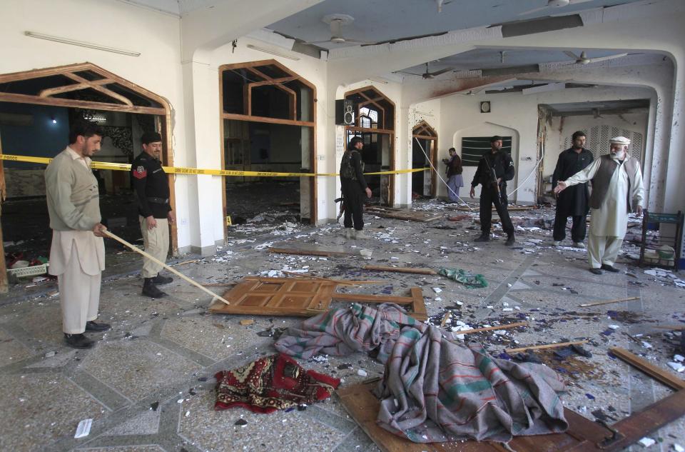 Men and security officials stand amidst debris after an explosion in a Shi'ite mosque in Peshawar