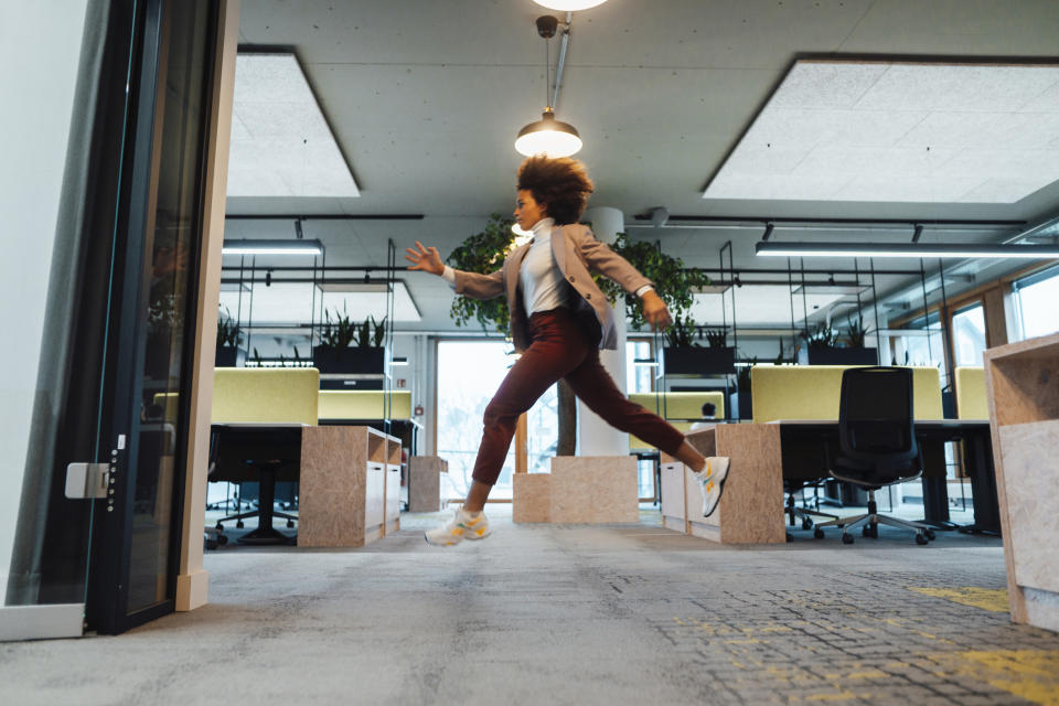 Person joyfully hopping inside a modern office with plants and desk cubicles in the background