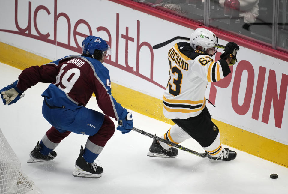 Colorado Avalanche defenseman Samuel Girard, left, reaches for the puck against Boston Bruins left wing Brad Marchand during the third period of an NHL hockey game Wednesday, Dec. 7, 2022, in Denver. Girard was called for tripping. (AP Photo/David Zalubowski)