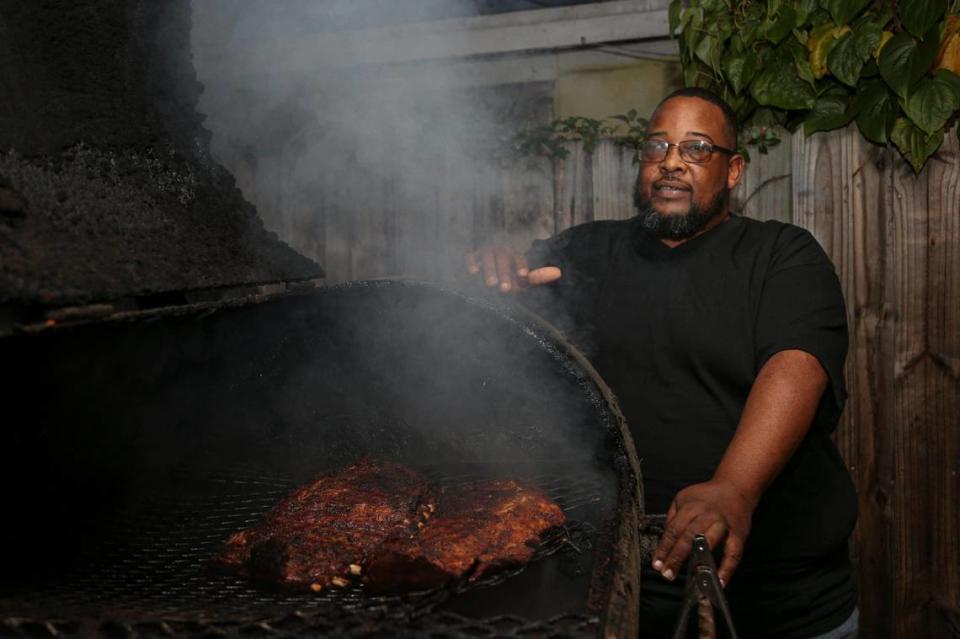 Larry D Reaves, 53, owner of World’s Famous Souseman BBQ, stands next to a grilling slab of pork ribs in the backyard of his Opa-locka home in Florida, Saturday, Nov. 19, 2022.