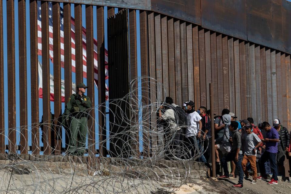 <p>Central American migrants look through a border fence as a US Border Partol agents stands guard near the El Chaparral border crossing in Tijuana, Baja California State, Mexico, on November 25, 2018.</p>
