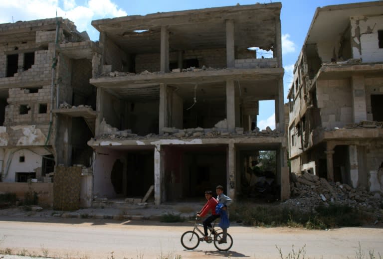 Syrian children ride a bicycle past destroyed buildings in a rebel-held area in the southern Syrian city of Daraa on June 3, 2018