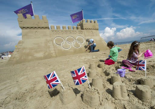 Children play in the sand while sculptor Mark Anderson puts the finishing touches to a giant sandcastle adorned with the Olympic rings and flags built to celebrate 100 days to go to the 2012 London Olympic Games on the beach at Weymouth on April 13, 2012. AFP PHOTO / ADRIAN DENNIS